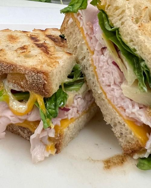 Close-up of a toasted sandwich with turkey, cheese, lettuce, and sliced vegetables, cut in half on a white plate.