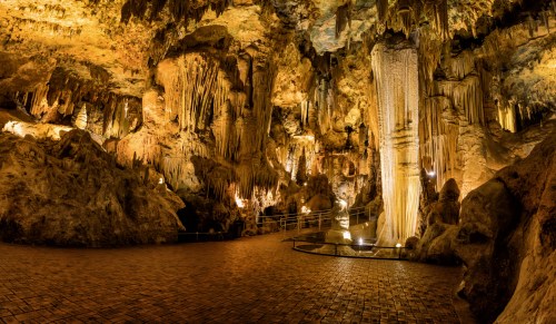 A stunning cave interior with stalactites and stalagmites, illuminated by soft lights, showcasing natural rock formations.