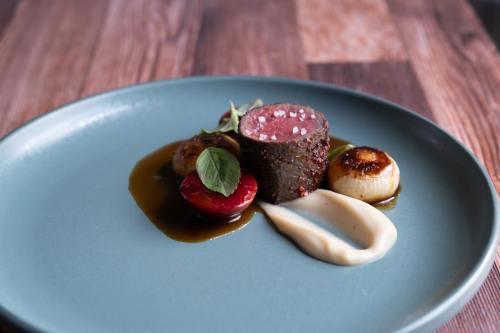 A gourmet dish featuring a round piece of meat, garnished with vegetables and sauces on a blue plate.