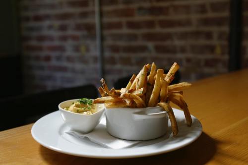 A plate with a serving of crispy fries in a white bowl and a small dish of creamy dip, set on a wooden table.