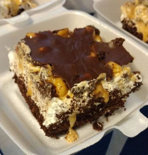 A close-up of a chocolate dessert bar with layers of cream, caramel, and a chocolate topping in a takeout container.
