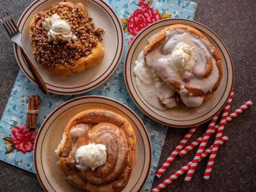 Three delicious cinnamon rolls on plates, topped with icing and ice cream, arranged on a floral tablecloth.