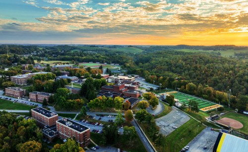 Aerial view of a college campus at sunset, surrounded by green hills and sports fields.