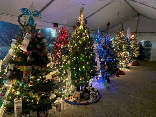 A festive display of decorated Christmas trees under a tent, illuminated with colorful lights and various ornaments.