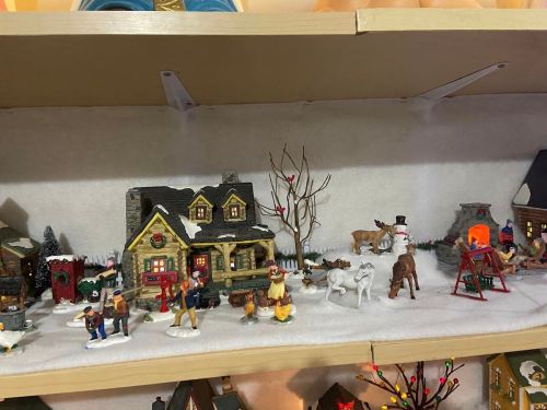 A festive display of miniature houses, figures, and animals on a snowy shelf, creating a winter scene.