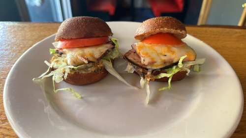 Two small sliders on a plate, featuring grilled chicken, melted cheese, lettuce, and tomato on mini buns.