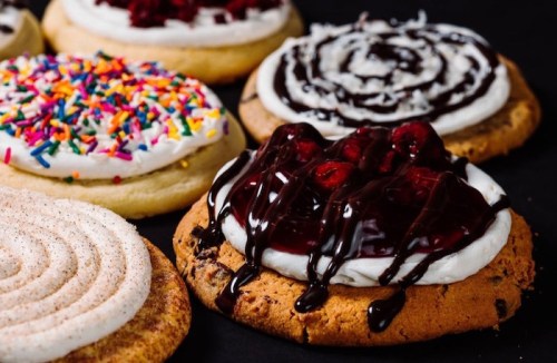 A variety of decorated cookies with frosting, sprinkles, and chocolate drizzle on a dark background.