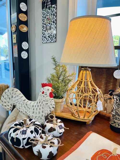 A cozy display featuring a woven lamp, a decorative chicken, and cow-print pumpkins on a wooden table.