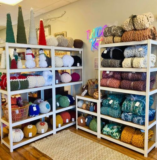 Shelves filled with colorful knitted items, including snowmen, trees, and various textured round pieces. Cozy shop display.