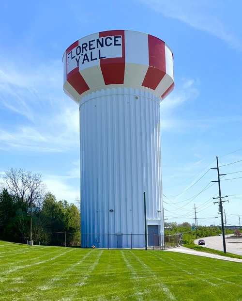 A tall water tower with red and white stripes, labeled "FLORENCE Y'ALL," surrounded by green grass and blue sky.