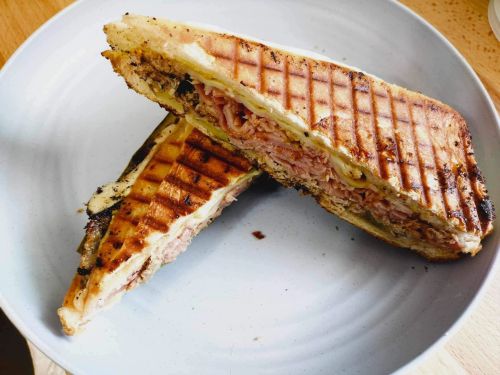 A grilled sandwich cut in half, revealing layers of ham and cheese, on a white plate.