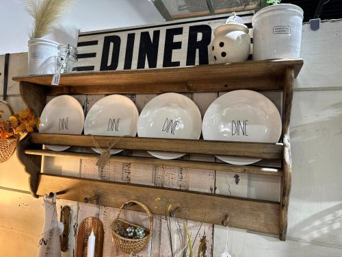 A wooden shelf displaying white plates labeled "DINE," with a vintage diner sign above and decorative items nearby.