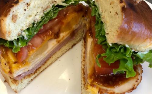 A close-up of a sandwich with layers of lettuce, tomato, cheese, ham, and chicken on a toasted bun.