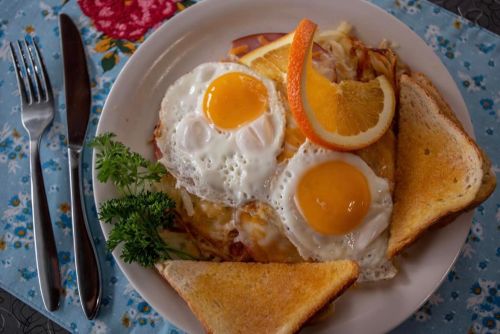 A plate of breakfast featuring two sunny-side-up eggs, toast, orange slices, and hash browns, on a floral tablecloth.