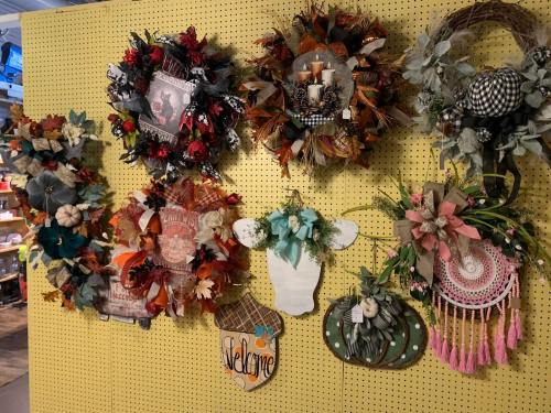 A display of various decorative wreaths in autumn colors, featuring flowers, leaves, and seasonal accents on a pegboard.