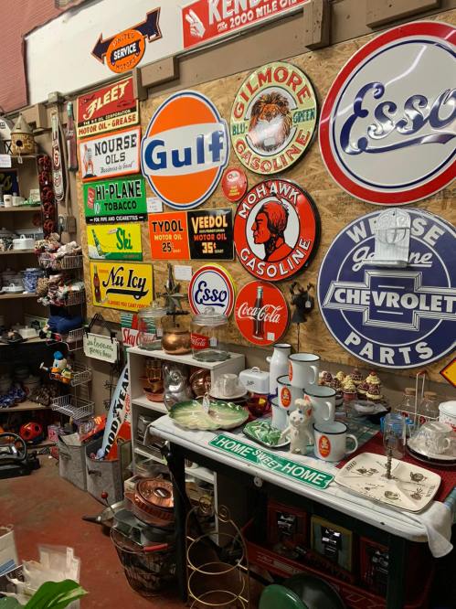 A vintage display featuring various gas station signs, collectibles, and a table with mugs and decor items.