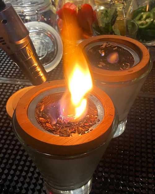 A close-up of two glass containers with wooden lids, one emitting a flame from a lit substance inside.