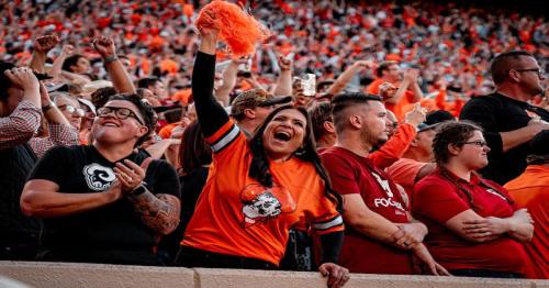 A lively crowd at a sports event, with fans cheering and celebrating in orange and black attire.