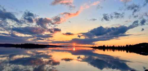 A serene sunset over a calm lake, with vibrant clouds reflecting on the water's surface.