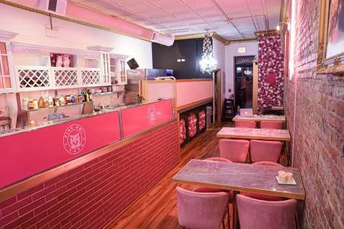 A cozy café interior with pink decor, a counter, and tables set for customers. Warm lighting enhances the inviting atmosphere.