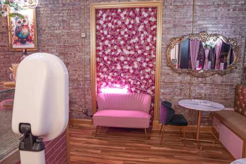 A cozy interior featuring a pink sofa, floral wall, and elegant mirror against a brick backdrop.