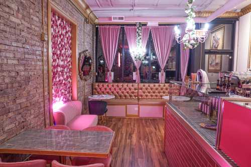 Cozy café interior with pink decor, tufted seating, and elegant lighting, featuring a marble table and floral accents.