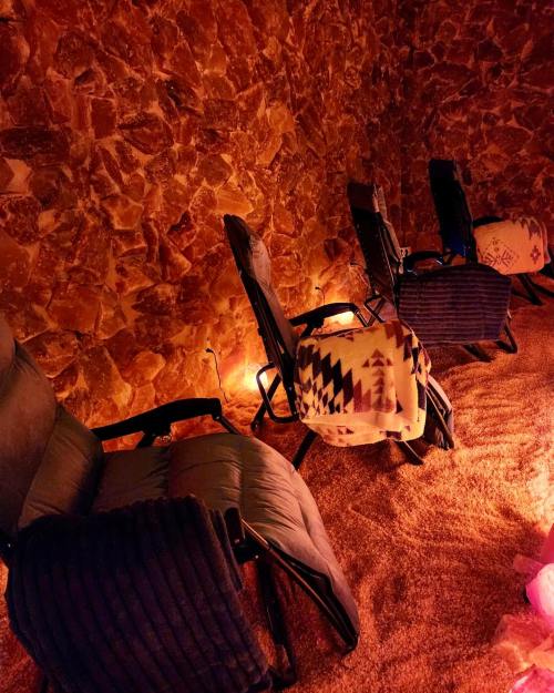 Cozy salt room with three reclining chairs, warm lighting, and textured stone walls. Soft blankets draped over chairs.
