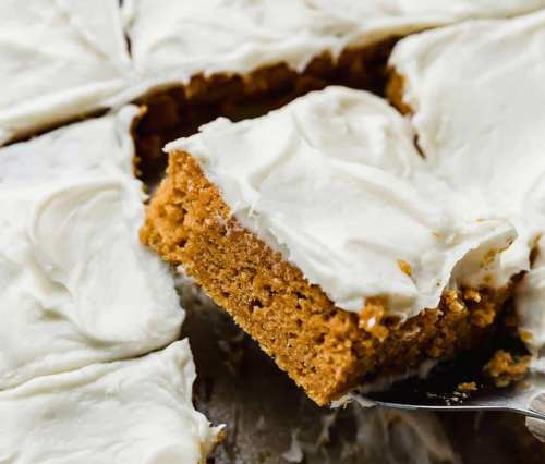 A slice of frosted pumpkin cake on a spatula, with the rest of the cake in the background.