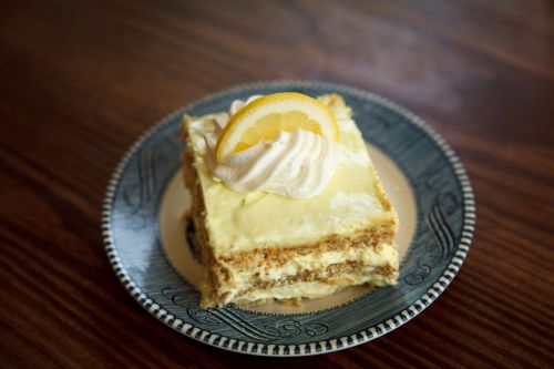 A slice of lemon dessert topped with whipped cream and a lemon slice, served on a decorative plate.