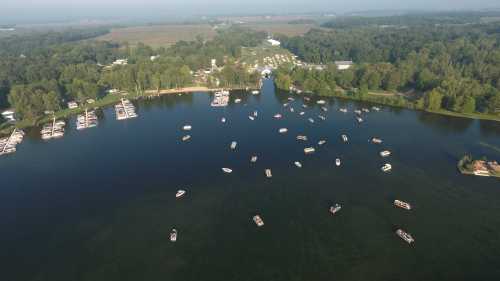 Aerial view of a serene lake with numerous boats and lush greenery surrounding the shoreline.