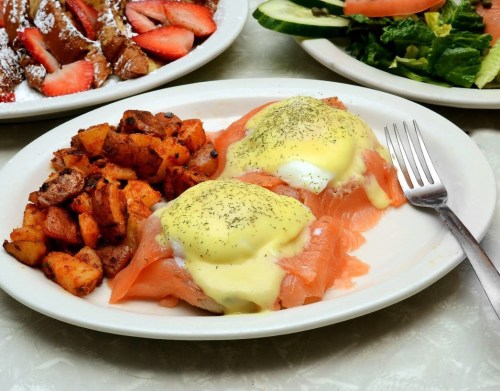 A plate of eggs Benedict with smoked salmon, hollandaise sauce, and seasoned potatoes on the side.