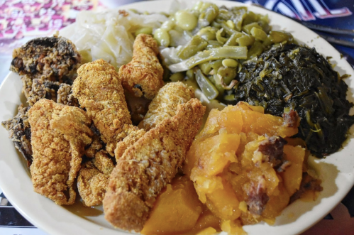 A plate of Southern comfort food featuring fried fish, collard greens, green beans, cabbage, and sweet potatoes.