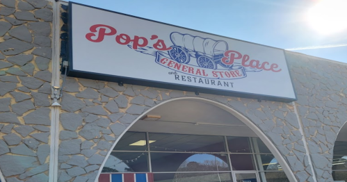 Sign for "Pop's Place General Store and Restaurant" on a stone wall, featuring a wagon graphic.