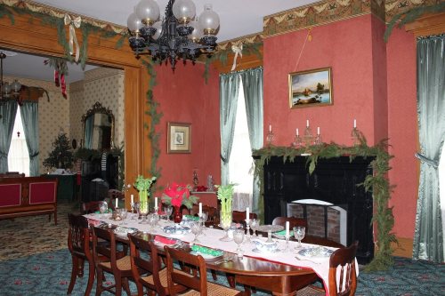 A festive dining room with a long table set for a meal, decorated with greenery and candles, featuring vintage decor.