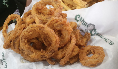 A pile of crispy, golden-brown onion rings on a white paper with a logo.