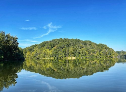 A serene lake reflecting a lush green island under a clear blue sky.