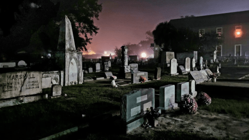 A dimly lit cemetery at night, featuring various gravestones and a foggy atmosphere.