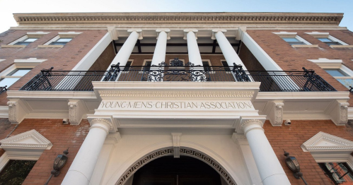 Facade of a historic building featuring tall columns and a balcony, with "Young Men's Christian Association" inscribed above the entrance.