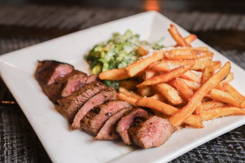 A plate featuring sliced steak, crispy fries, and a side of chopped greens with cheese.