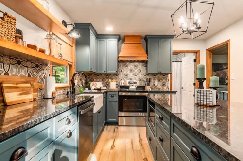 Modern kitchen with blue cabinets, a black countertop, patterned backsplash, and wooden accents. Bright and inviting space.