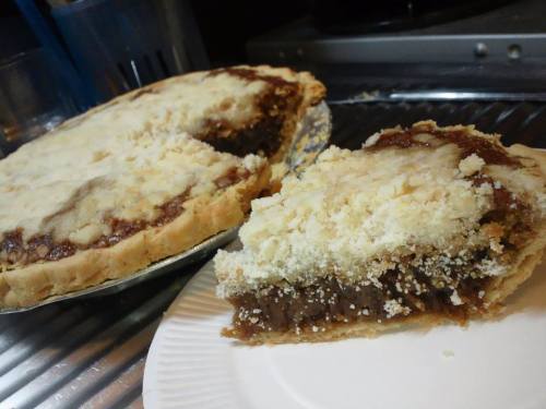 A freshly baked pie with a crumbly top, partially sliced, sitting on a plate next to the whole pie.
