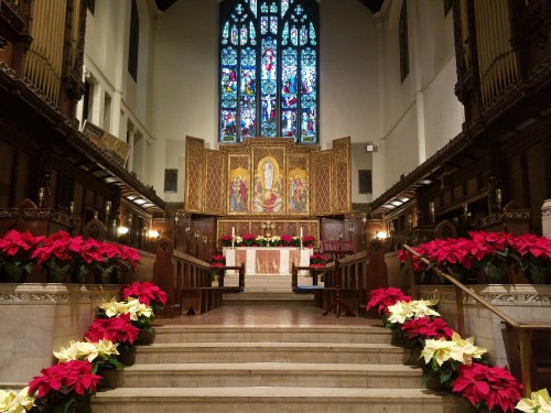 Interior of a church with a decorated altar, colorful stained glass windows, and poinsettias lining the steps.