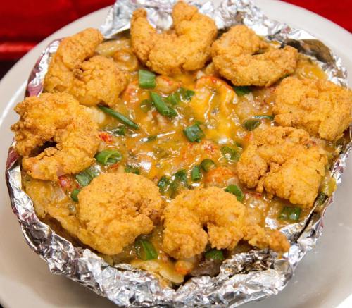 A foil-wrapped dish topped with golden fried shrimp, green onions, and a creamy sauce over a bed of rice or pasta.