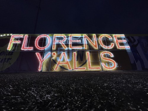 Neon sign reading "FLORENCE Y'ALLS" illuminated against a dark background.