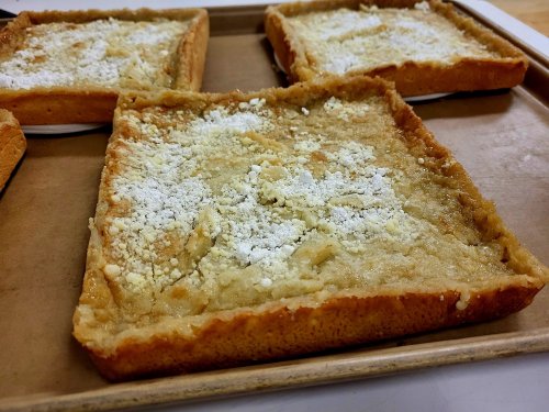 A close-up of square dessert bars dusted with powdered sugar on a baking tray.