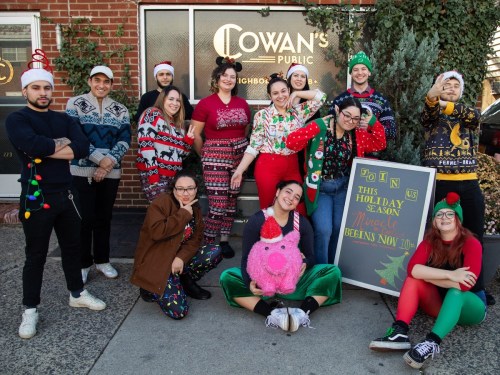 A festive group of people in holiday attire poses outside a pub, smiling and celebrating the season.