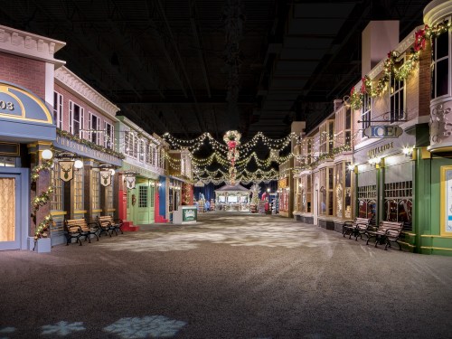 A festive street scene with decorated storefronts, benches, and holiday lights, creating a cheerful atmosphere.