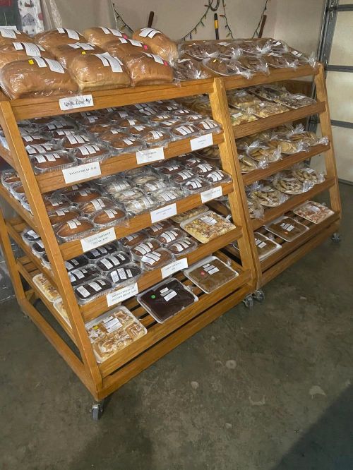 Two wooden racks filled with various baked goods, including loaves of bread and assorted pastries, in a storage area.
