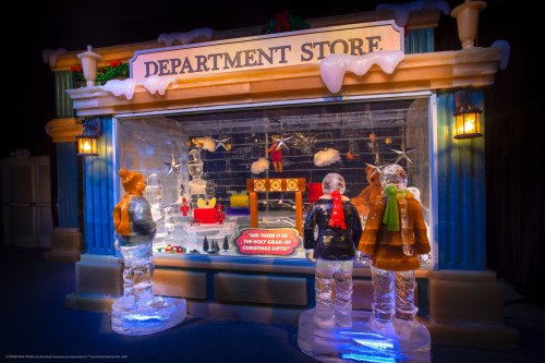 A festive ice sculpture display featuring a department store window with holiday decorations and gift-themed elements.