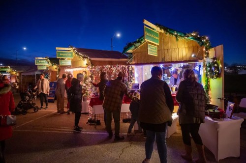 Festive market stalls illuminated at night, with people browsing and holiday decorations adorning the booths.